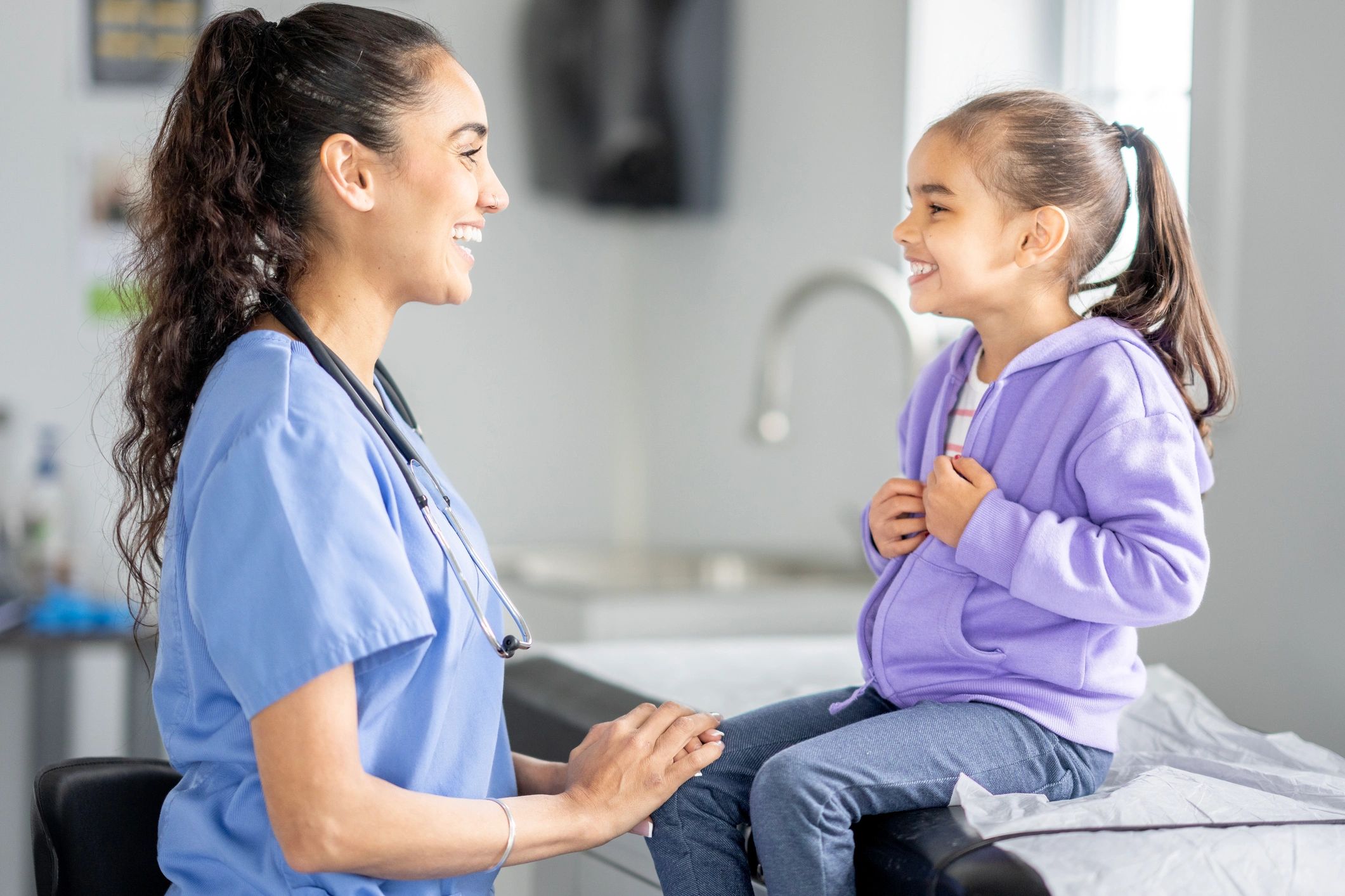 Smiling Hispanic Female Pediatric Nurse With Young Girl Patient in Clinic Exam Room